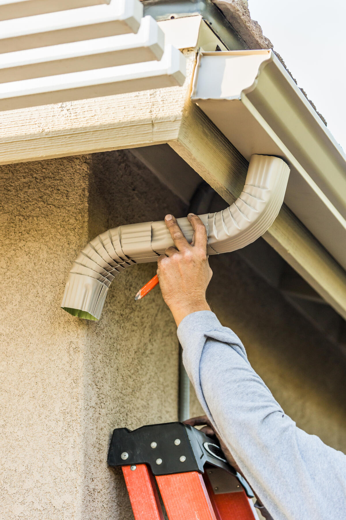 Professional installing seamless gutters on a residential home in Albuquerque. Downspout A