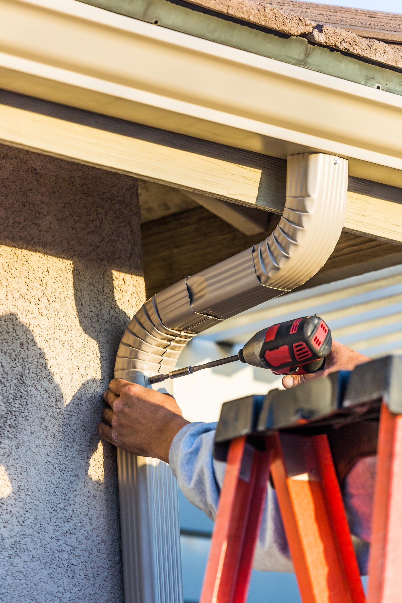 Professional installing seamless gutters on a residential home in Albuquerque. Downspout screw.