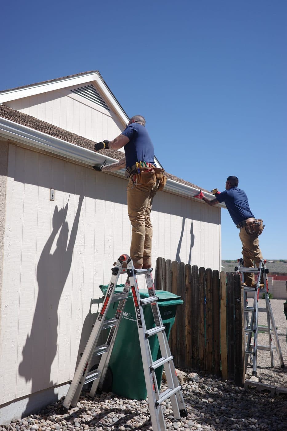 Crew installing new gutters from ladders on a stucco Albuquerque home