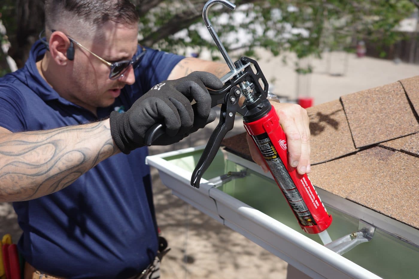 Technician sealing a seamless gutter joint with a caulk gun