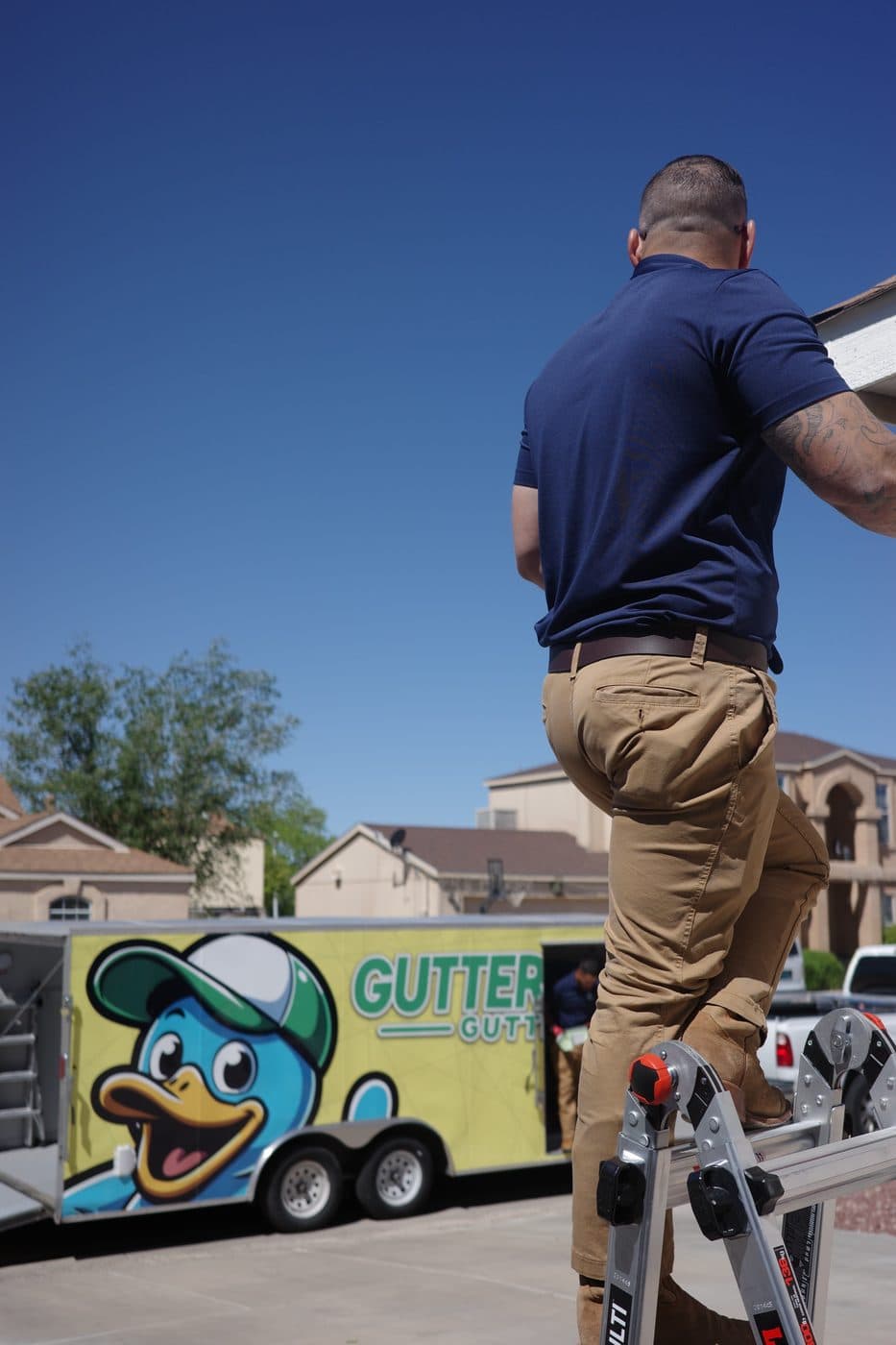 Technician carrying a gutter section up to the roofline by the branded trailer