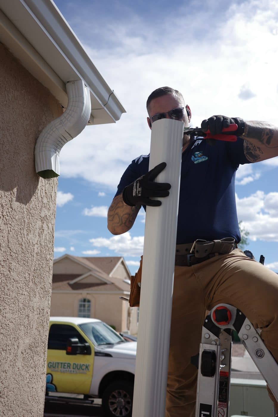 Technician installing a downspout from a ladder with the branded truck in view